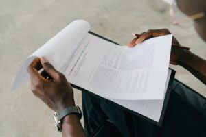 Hands holding and reviewing business documents with a pen, focusing on detailed paperwork.
