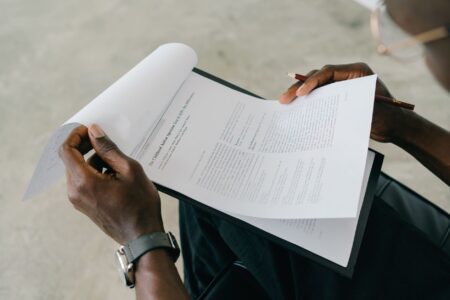 Hands holding and reviewing business documents with a pen, focusing on detailed paperwork.