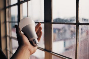 Eine Hand hält eine LED-Glühbirne nahe einem Fenster und symbolisiert Energieeffizienz.