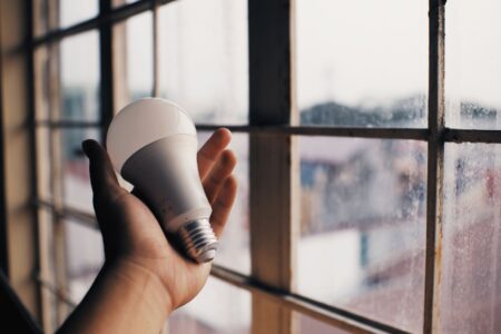 Eine Hand hält eine LED-Glühbirne nahe einem Fenster und symbolisiert Energieeffizienz.