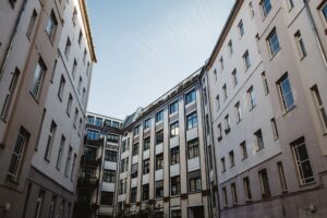 Ein hohes Wohngebäude in einem Stadtinnenhof mit klarem blauen Himmel darüber.