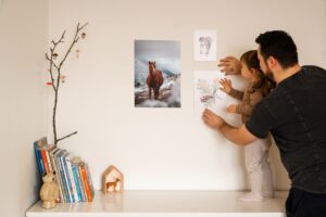 Ein Vater hilft seiner Tochter, Bilder an die Wand zu hängen und schafft eine warme und gemütliche Wohnatmosphäre.