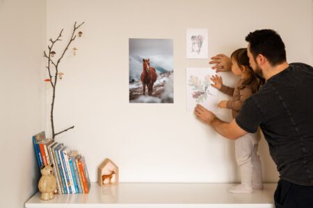 Ein Vater hilft seiner Tochter, Bilder an die Wand zu hängen und schafft eine warme und gemütliche Wohnatmosphäre.