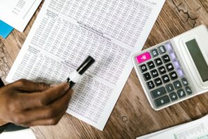 Nahaufnahme von Steuerdokumenten und Taschenrechner auf einem Holztisch, der die Finanzanalyse hervorhebt.