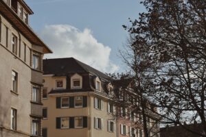 Aufnahme aus niedriger Perspektive von städtischen Wohngebäuden und Bäumen unter einem klaren blauen Himmel.