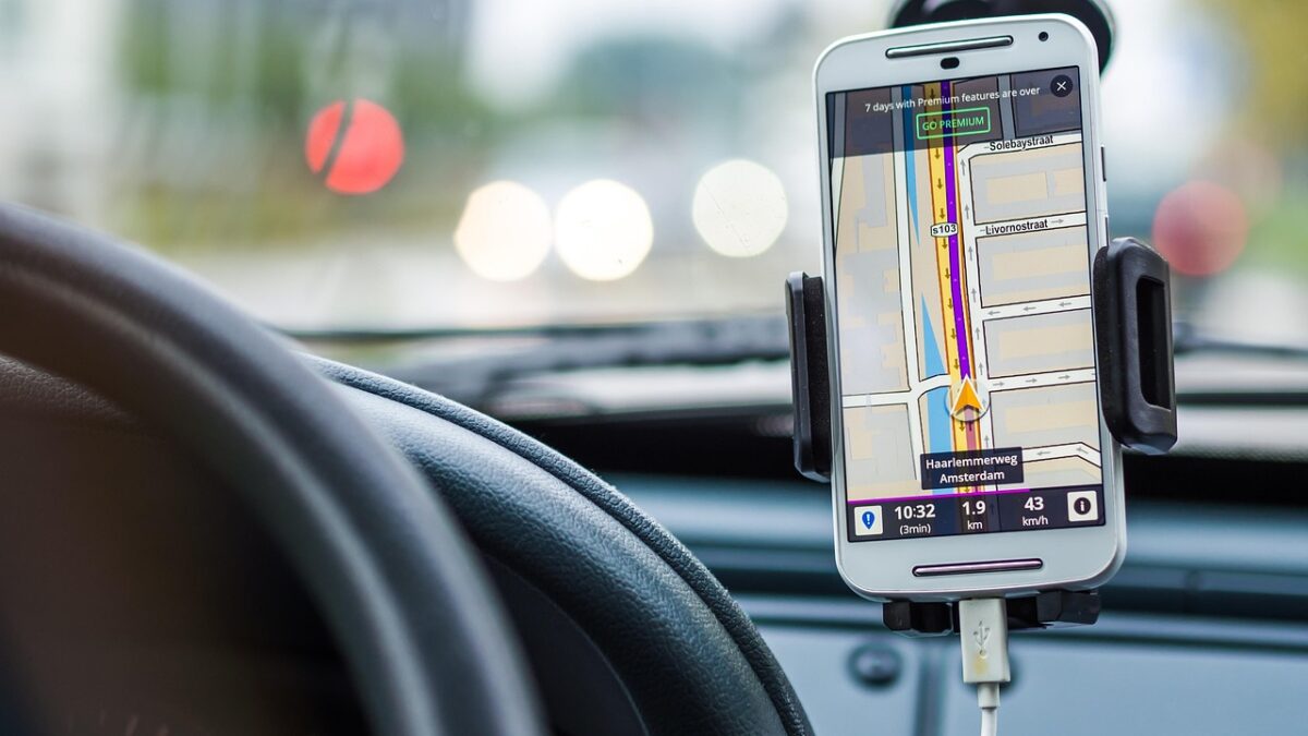 Smartphone auf einer Halterung im Auto, das eine GPS-Navigations-App mit einer Stadtkarte zeigt (Haarlemmerweg, Amsterdam). Lenkrad und Windschutzscheibe unscharf im Hintergrund.